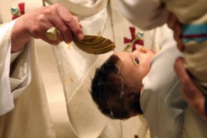 Baptême d'un bébé : le prêtre verse de l'eau sur le front d'un bébé porté par ses parents.